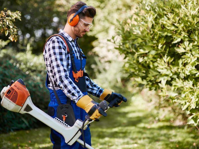Person using a string trimmer in a grassy yard, wearing orange earmuffs and safety gloves.