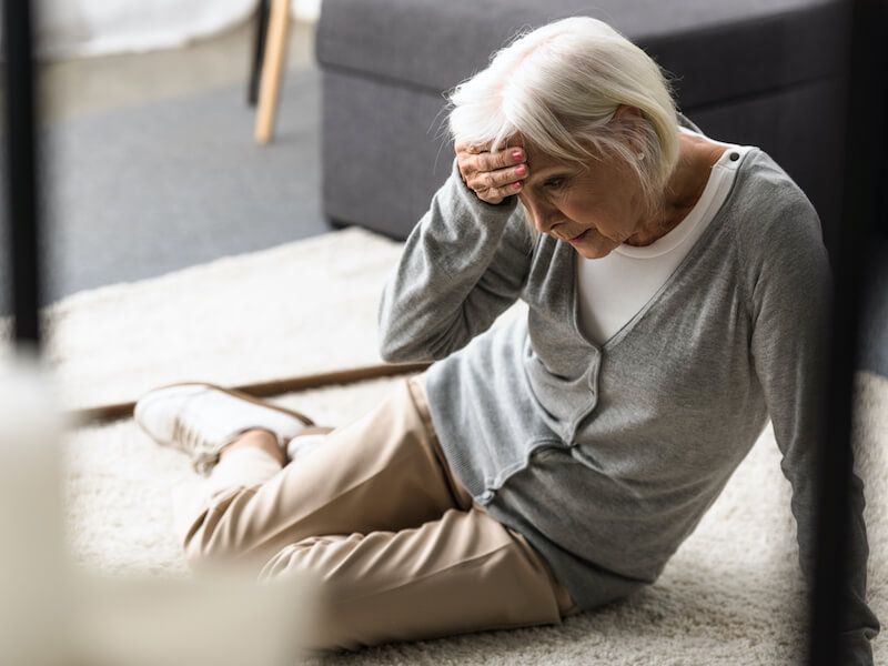 Person sitting on the floor, holding their head in apparent pain beside a sofa.