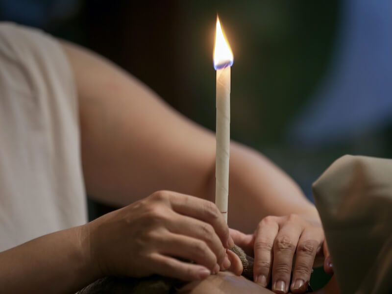 Hands holding a lit candle in a dim indoor setting