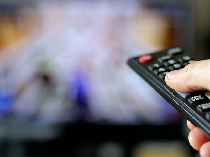 Hand holding a TV remote aimed at a blurred television screen