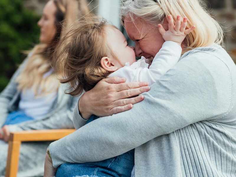 Woman hugging a child closely in a warm embrace, with another person blurred in the background