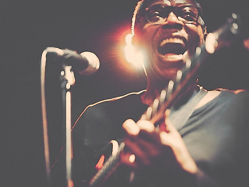 Singer passionately performing on stage with microphone and guitar, warm spotlight behind them
