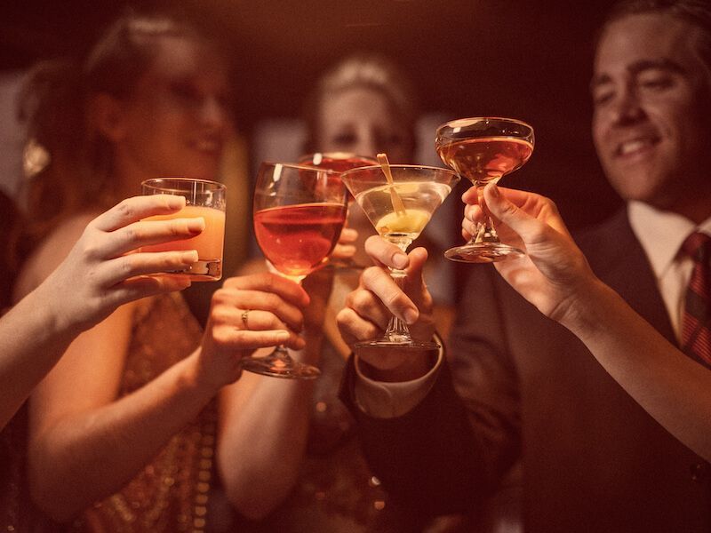 People raising cocktail glasses in a warm-lit celebratory toast