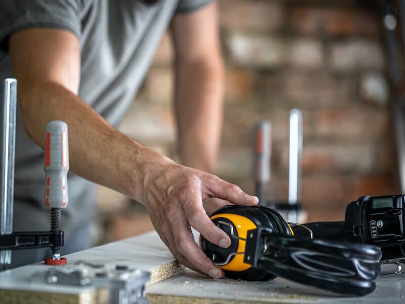 Person using a tape measure on a wooden board in a workshop, with clamps and tools nearby