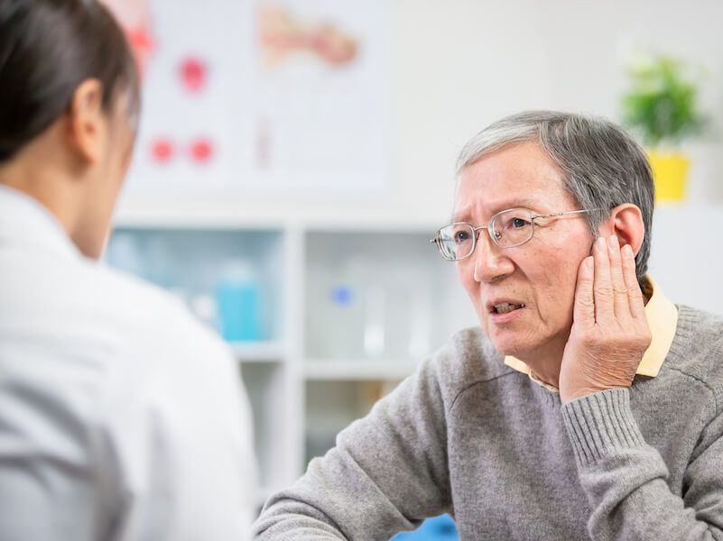 Doctor examining a patient who is holding her cheek in a bright clinic setting