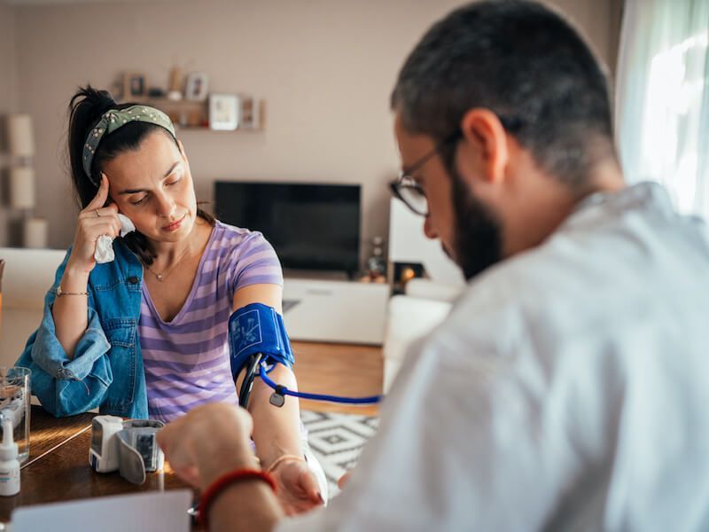 Person checking a blood pressure cuff on a seated patient at a kitchen table