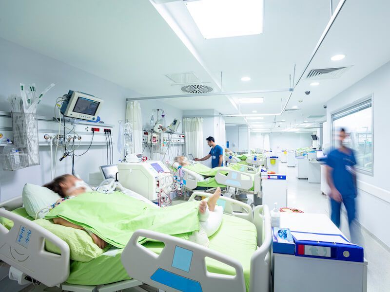 Hospital ward with patients in beds, monitors, and staff moving through a bright ICU room.