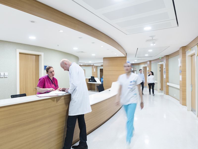 Bright hospital reception area with staff at the counter and people walking through the hallway