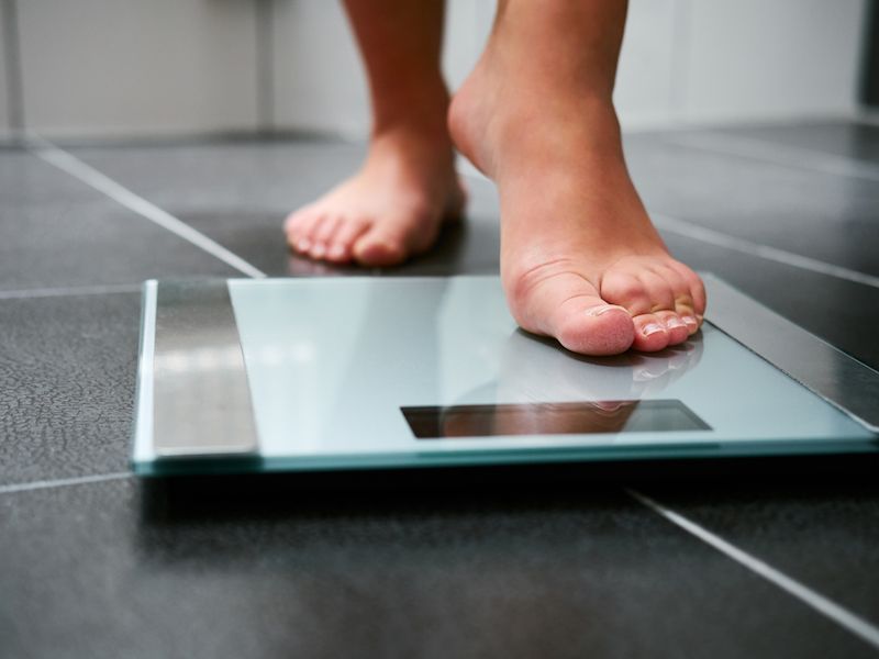 Bare feet standing on a digital bathroom scale on a tiled floor