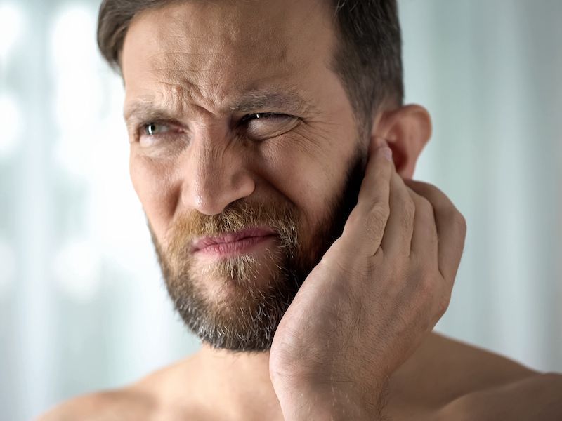 Man rubbing his cheek with a pained expression, suggesting tooth or jaw pain