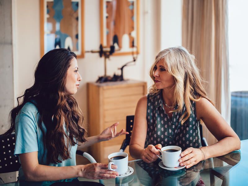 Two women talking at a table with coffee in a bright room