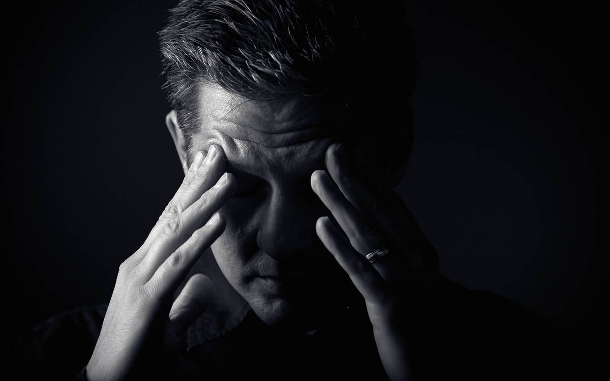 Man holding his temples in a dark, low-lit scene, appearing stressed or in pain