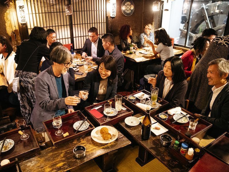 People dining together at a lively restaurant, sharing drinks and dishes around a crowded table.