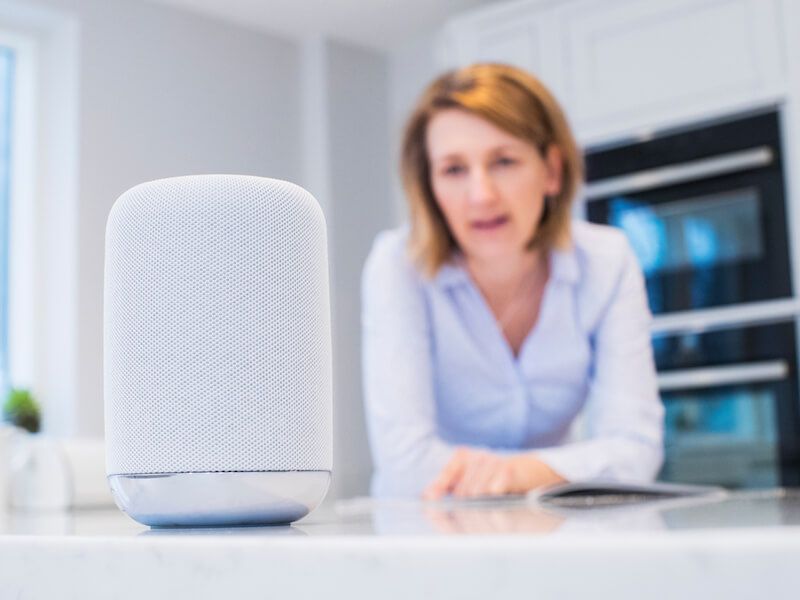 White smart speaker on a kitchen counter with a blurred person in the background