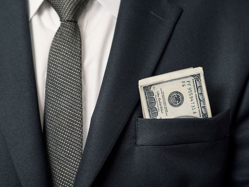 Close-up of a navy suit jacket with a money-filled breast pocket and patterned tie