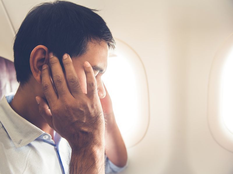 Man sitting by an airplane window with his hands covering his face, appearing stressed or tired
