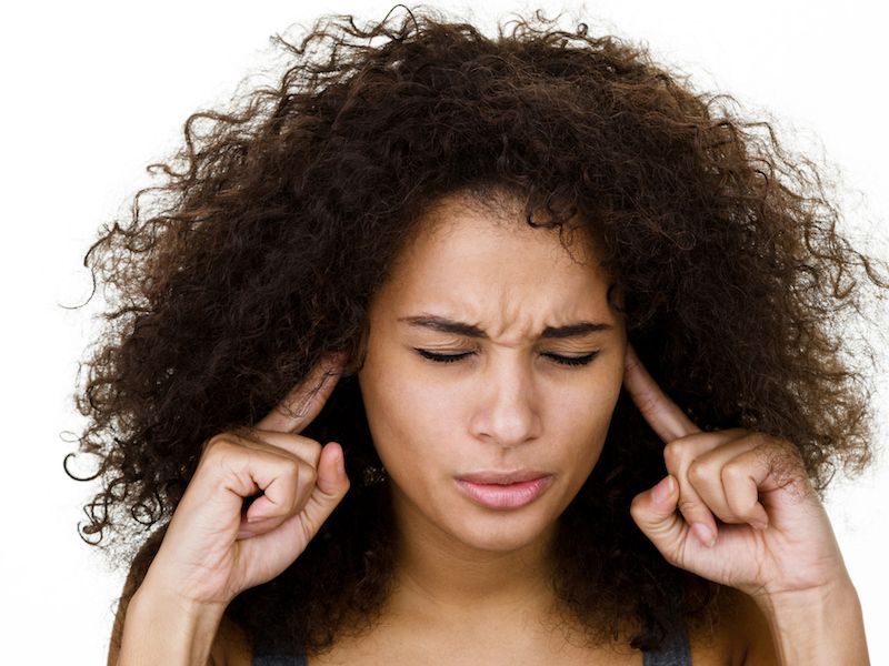 Woman with curly hair pressing her temples and closing her eyes, appearing frustrated or stressed