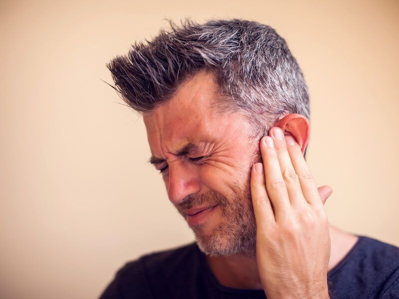 Man grimacing and holding his ear in pain against a plain background