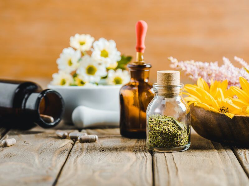 Assorted herbal remedy bottles and flowers arranged on a rustic wooden table