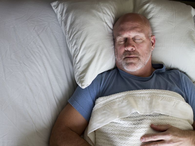 Sleeping man in a blue shirt lying in bed under a white blanket