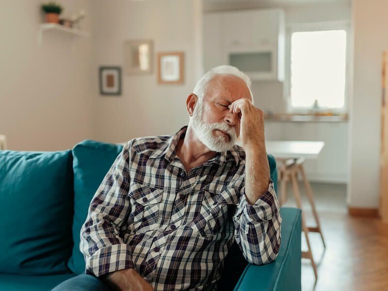 Man sitting on a teal couch, resting his head on his hand in a bright living room.