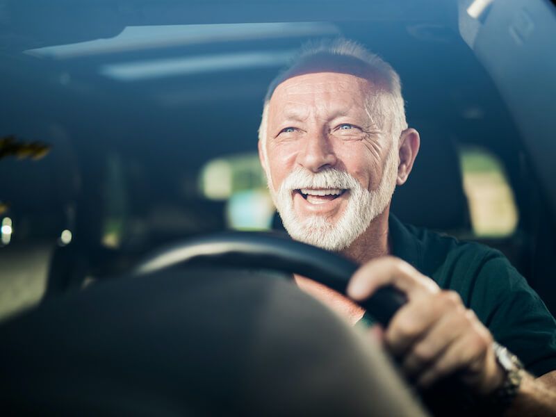 Smiling man driving a car, seen from the front with hands on the steering wheel.