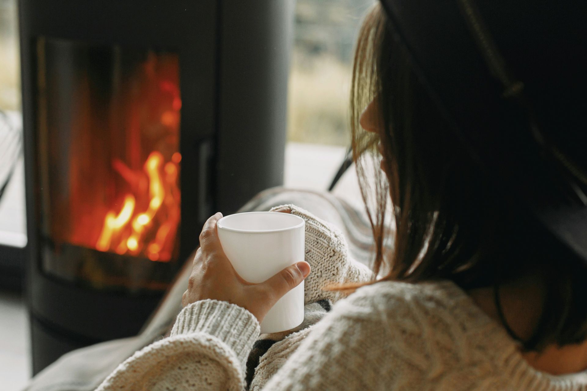 Personne avec une tasse de thé devant une cheminée à la maison en hiver