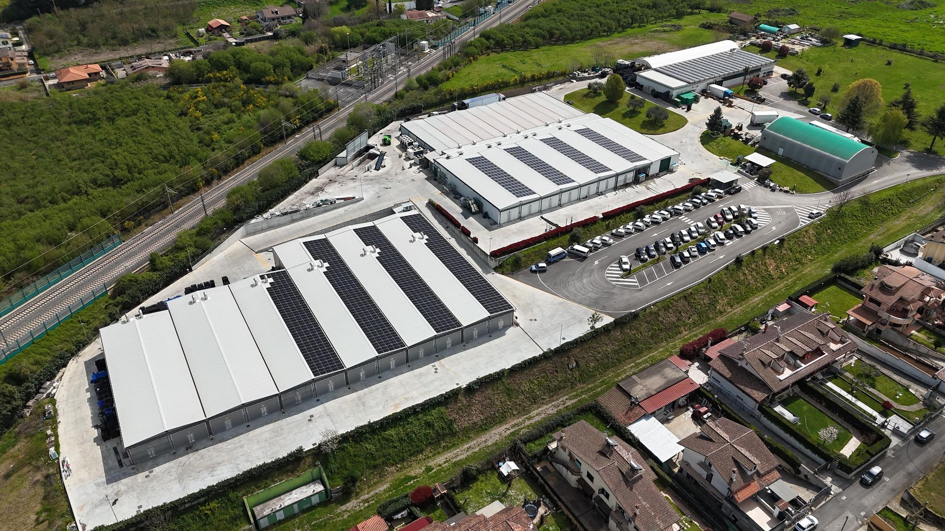 Vista aerea di un complesso industriale con più edifici, parcheggio e vegetazione circostante.