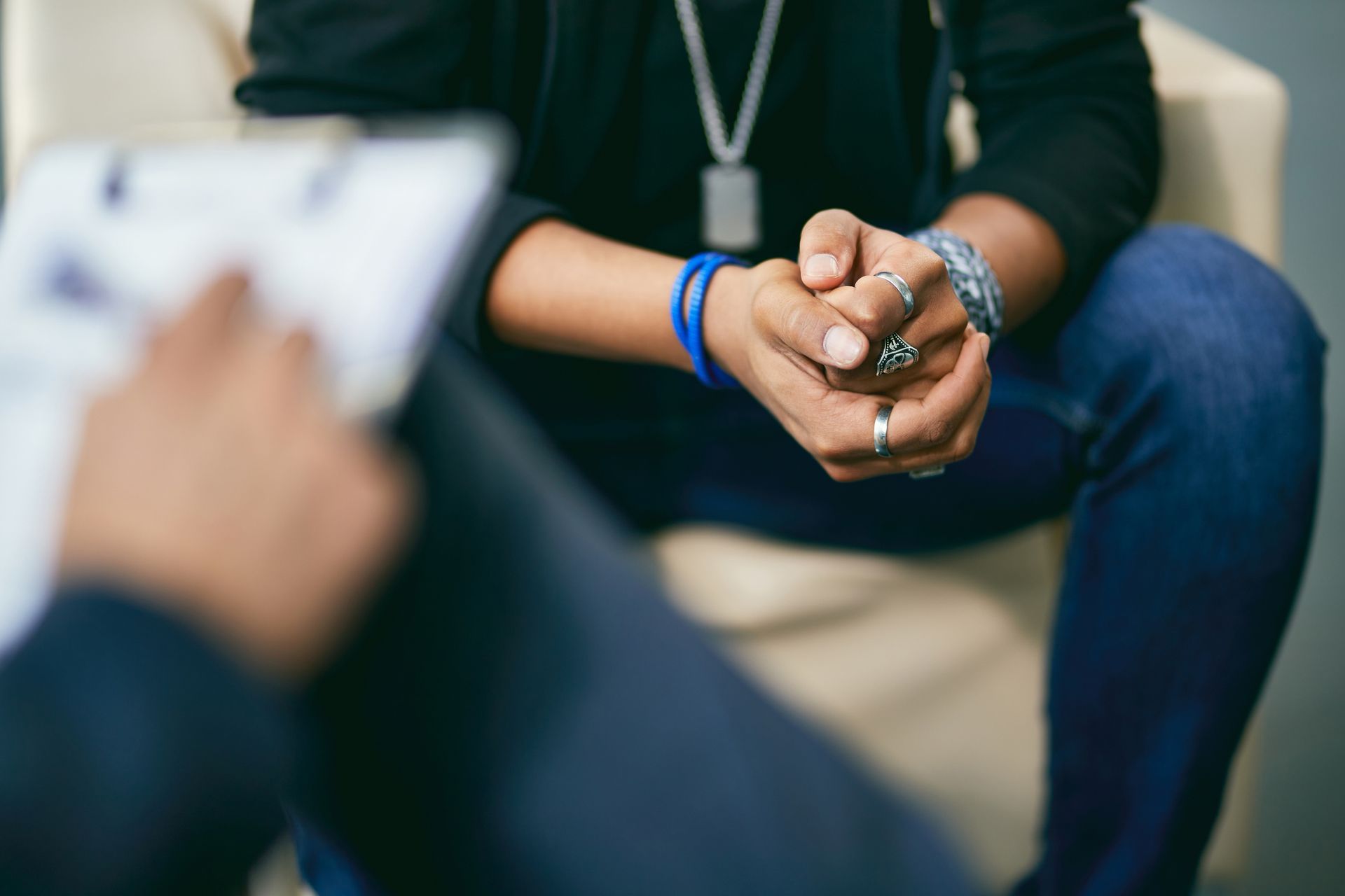 A person is sitting in a chair with their hands folded and talking to another person.