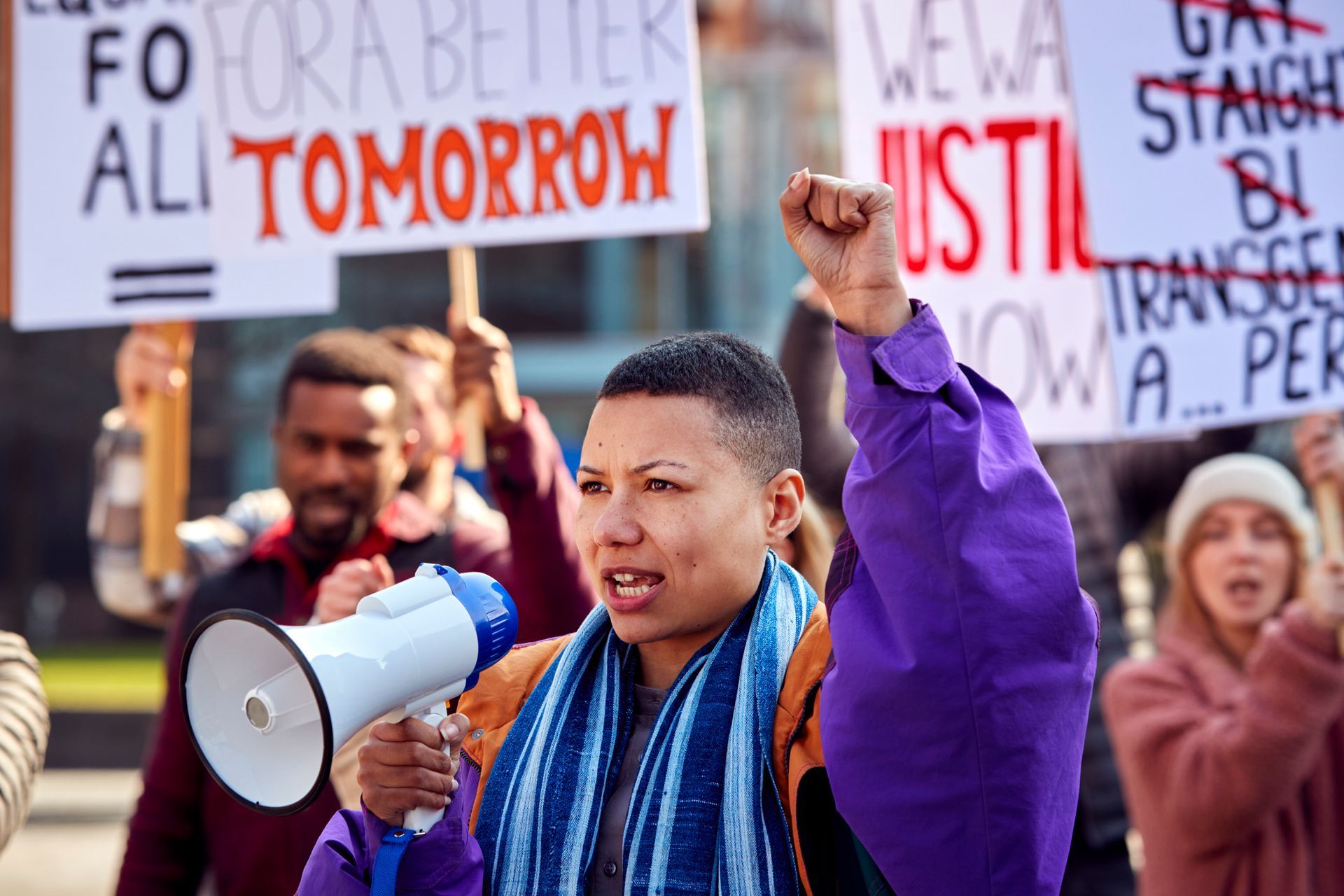 A woman is holding a megaphone in front of a crowd of people holding signs.