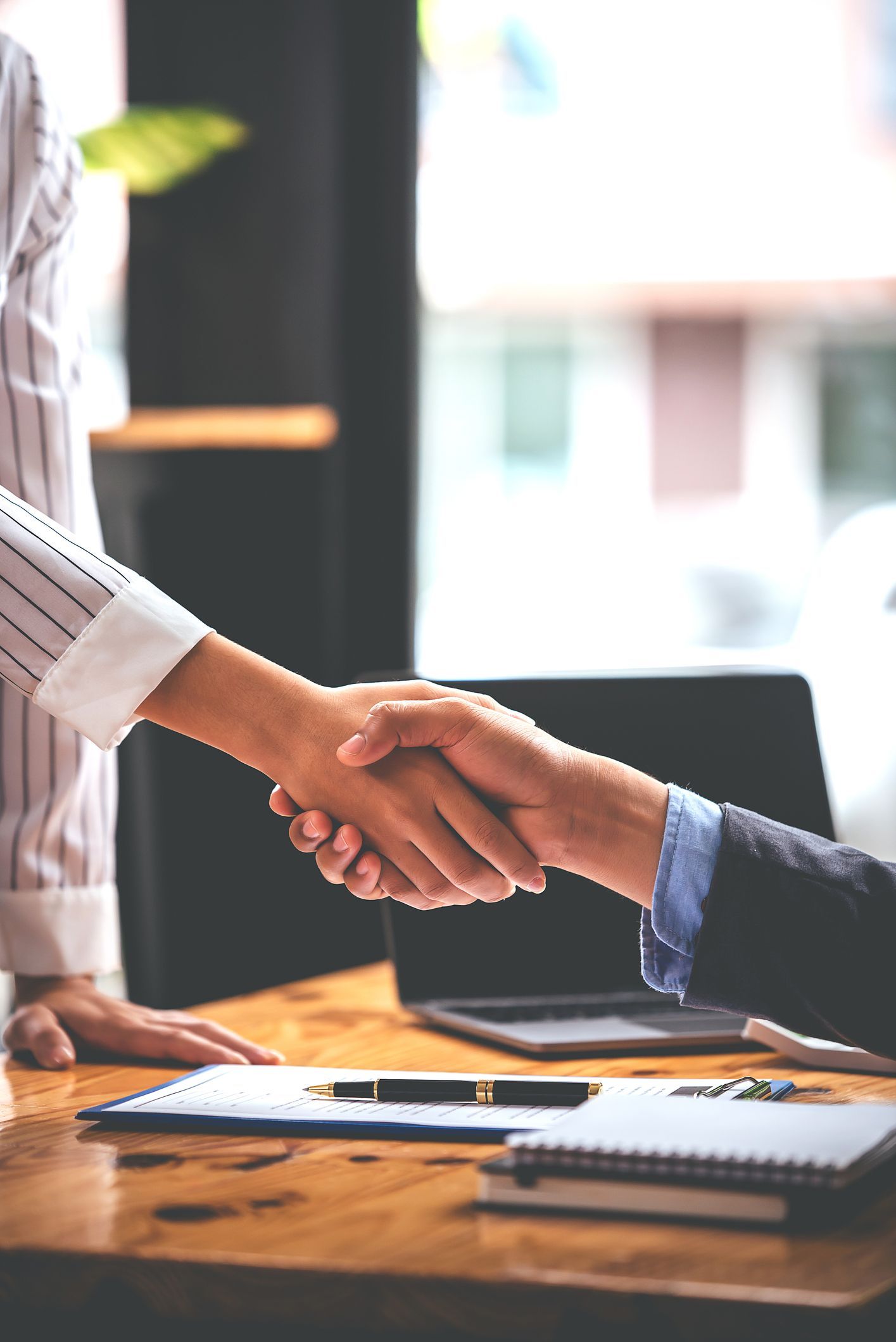 Two people are shaking hands over a wooden table.