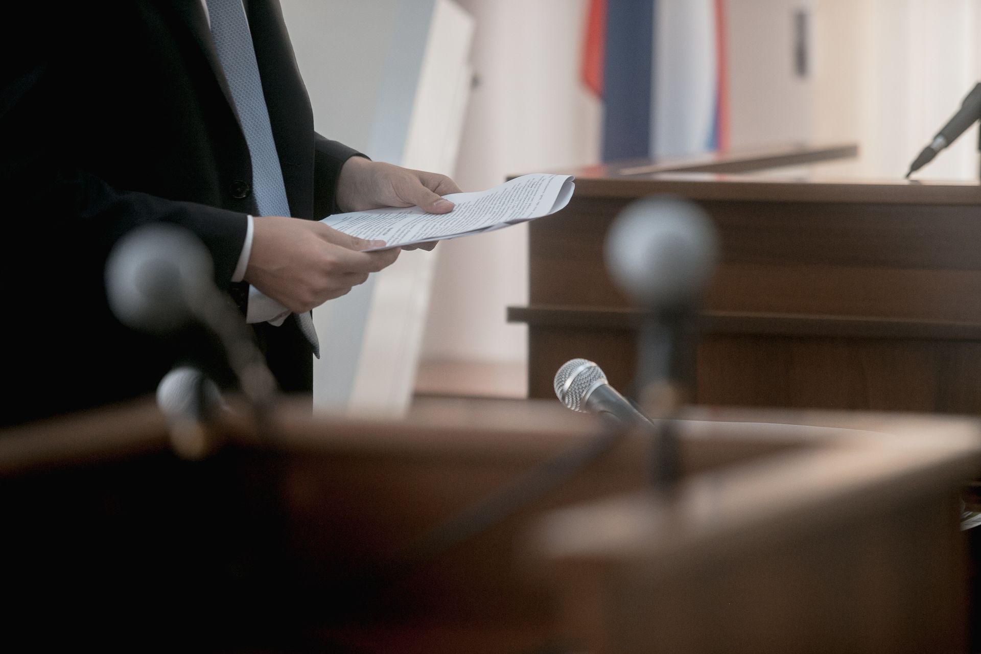 A man in a suit and tie is standing at a podium holding a piece of paper.