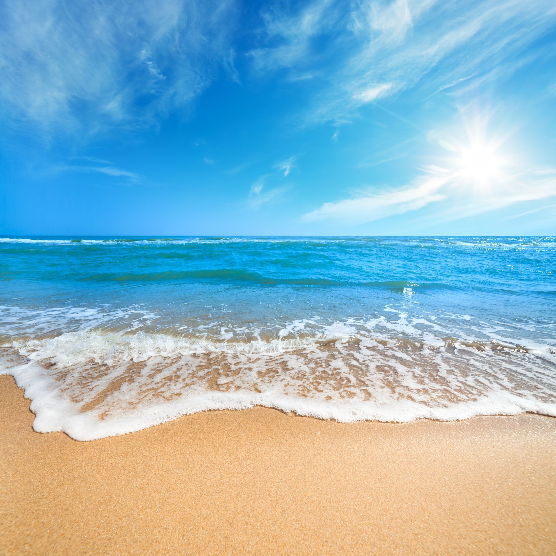 The sun is shining on the beach and the waves are coming in