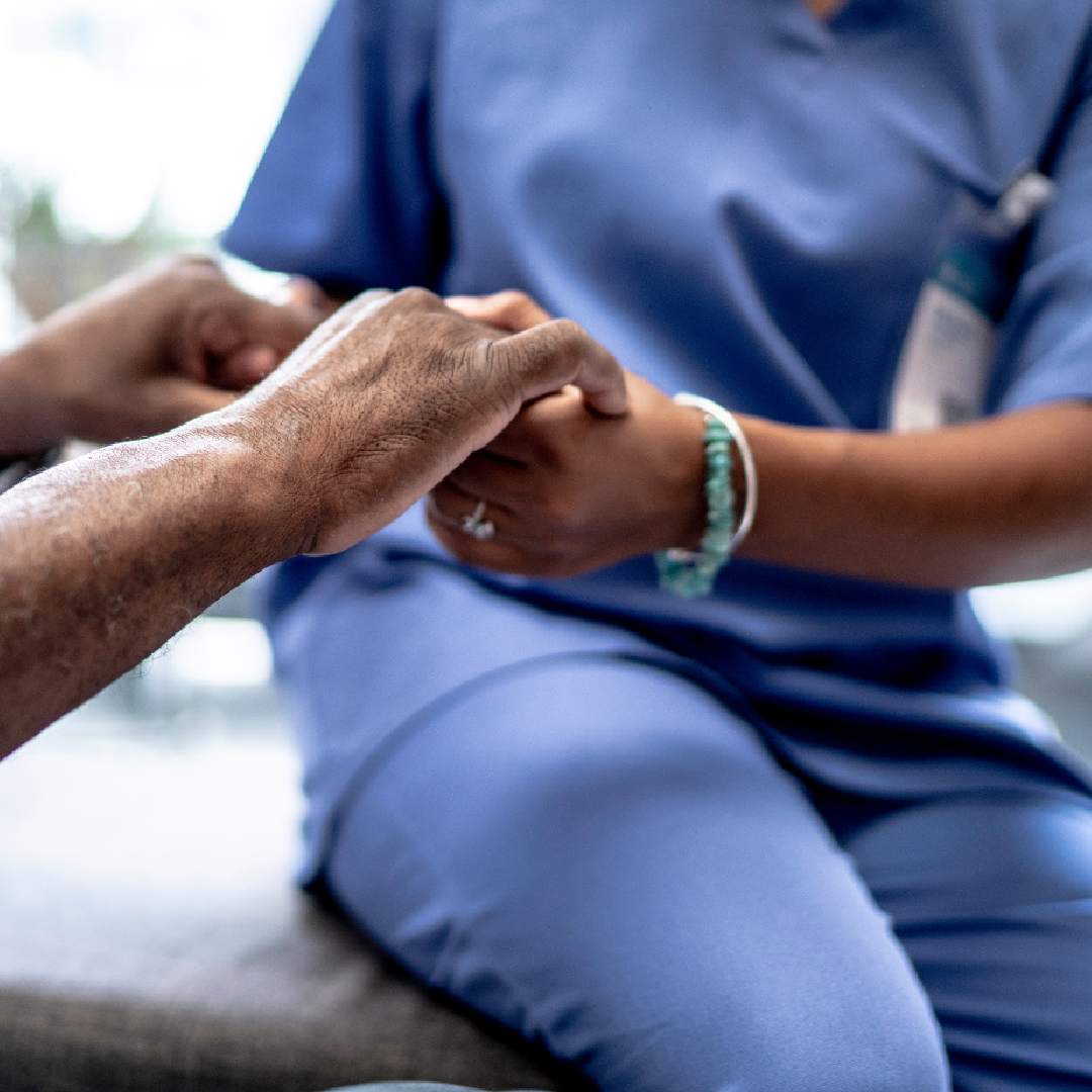 A nurse is holding a patient 's hand while sitting on a couch.