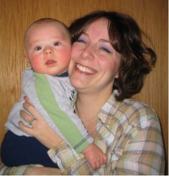 Smiling woman holding a baby indoors against a wooden wall