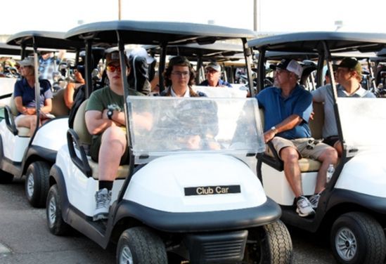 Golf carts filled with passengers lined up outdoors under a canopy