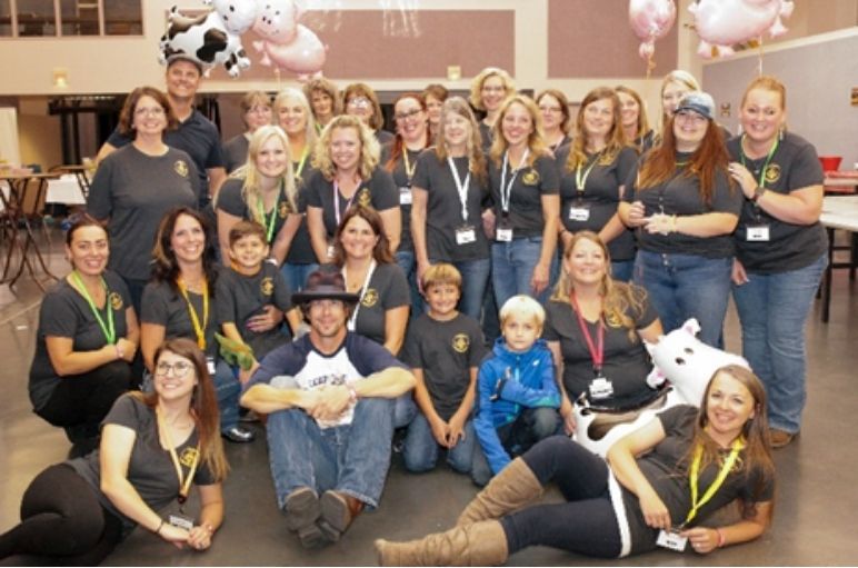 Group of people posing indoors at a festive event, with balloons and a cow-themed backdrop.
