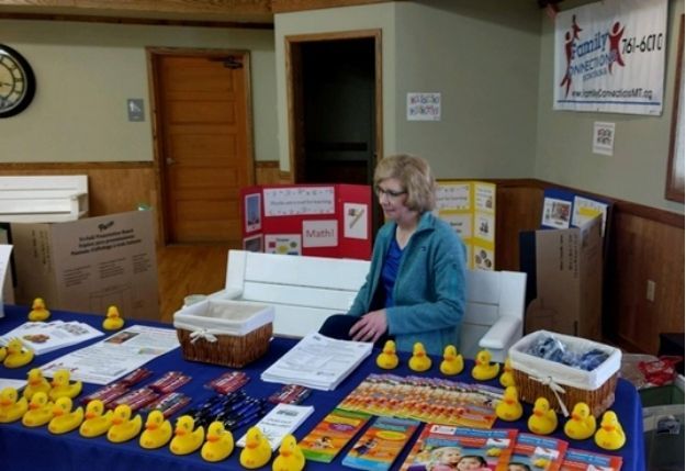 Woman at a table displaying many yellow rubber ducks at an indoor fair or market booth