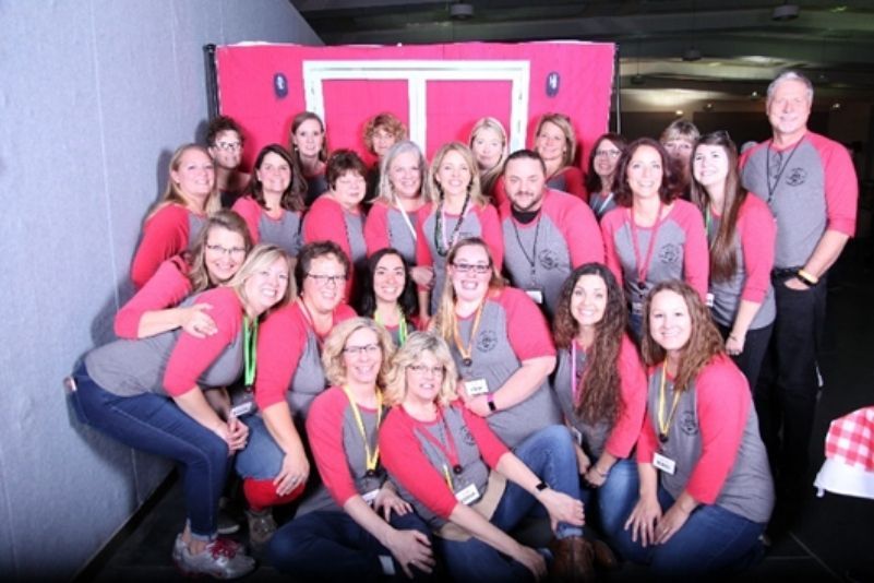 Group of people posing in matching pink shirts in front of a bright pink backdrop.