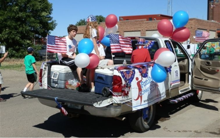 Decorated truck with balloons and patriotic signs in a parade, people standing in the back on a sunny street