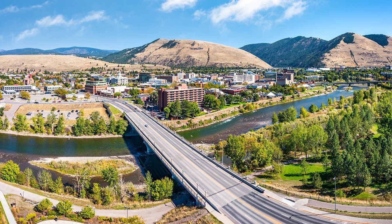 Bridge over river in a sunny mountain town with green trees and tan hills