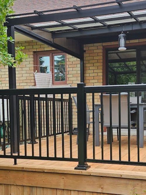 Une terrasse en bois avec une balustrade noire et une table et des chaises sous un auvent.