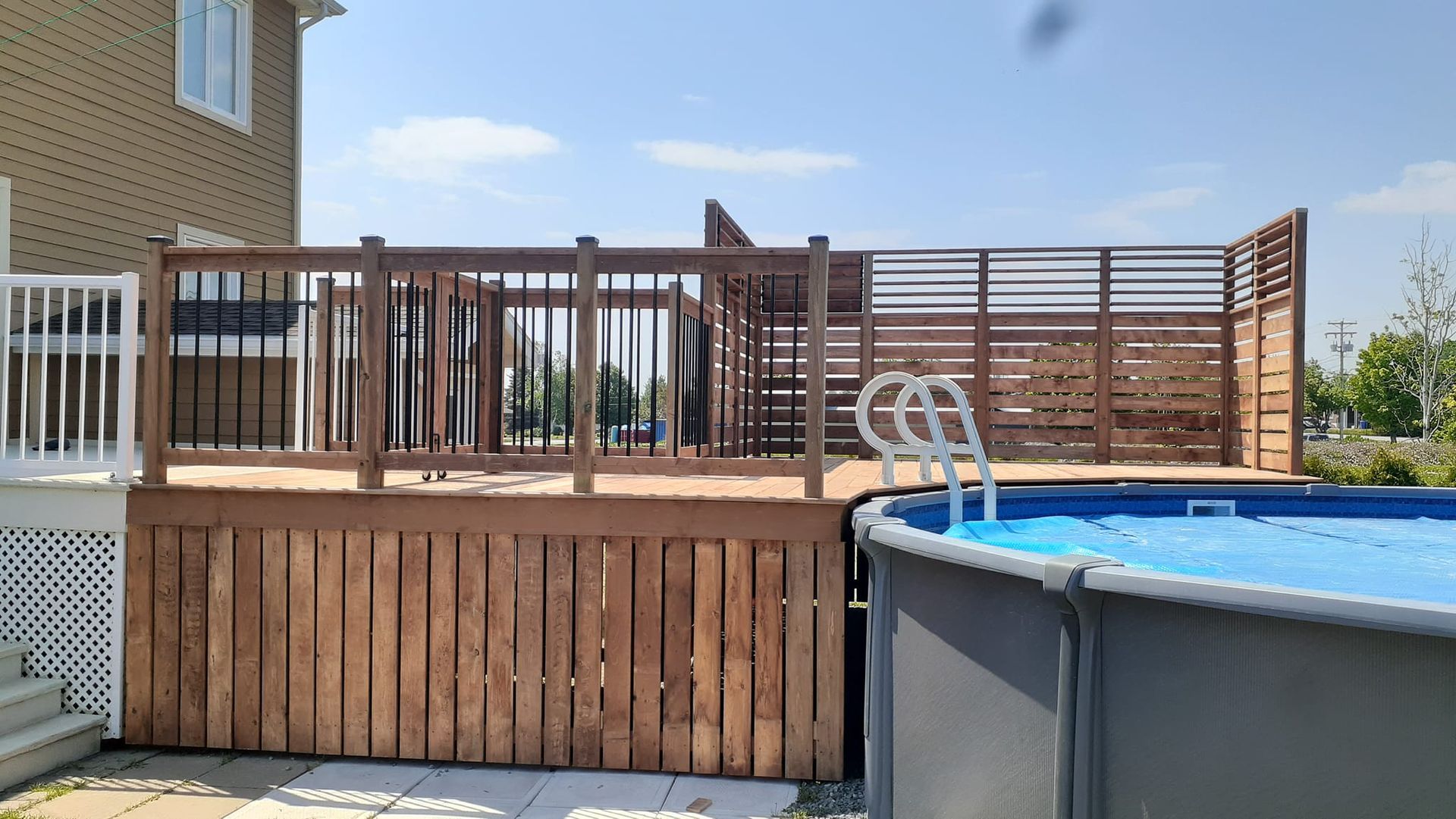 Une terrasse en bois à côté d'une piscine dans une cour arrière.