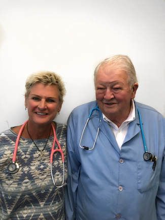 Two people in medical scrubs with stethoscopes, smiling against a plain background.