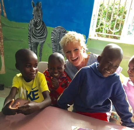 A smiling person surrounded by children at a table in a room with a painted zebra wall mural.