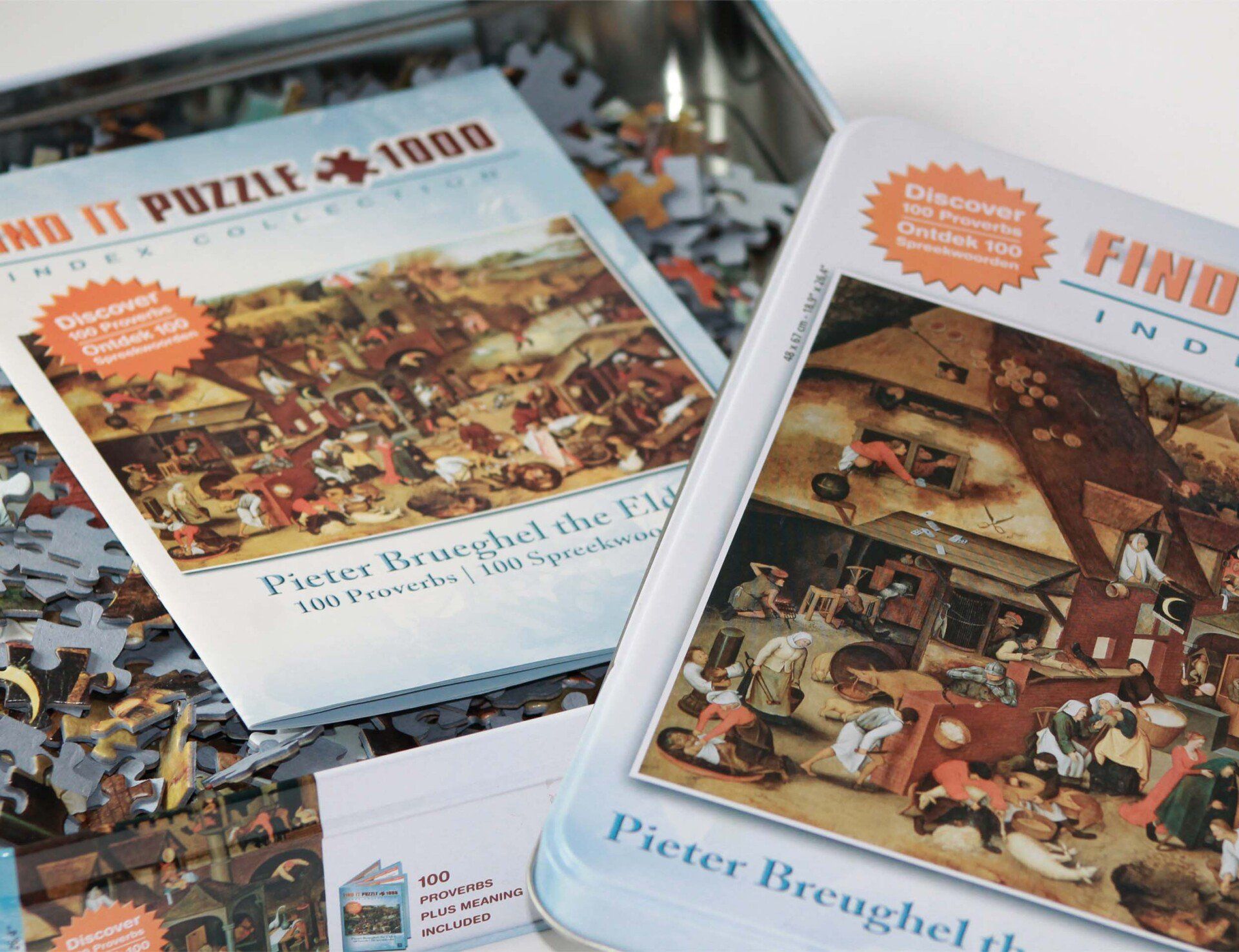 Twee open puzzelblikken met schilderijen van Pieter Bruegel de Oudere, omringd door losse puzzelstukjes.