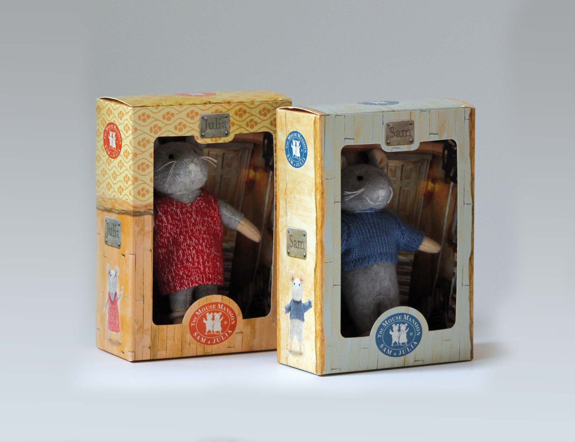 Twee knuffelmuizen in aparte kartonnen doosjes; de ene draagt ​​een rode jurk, de andere een blauwe trui.