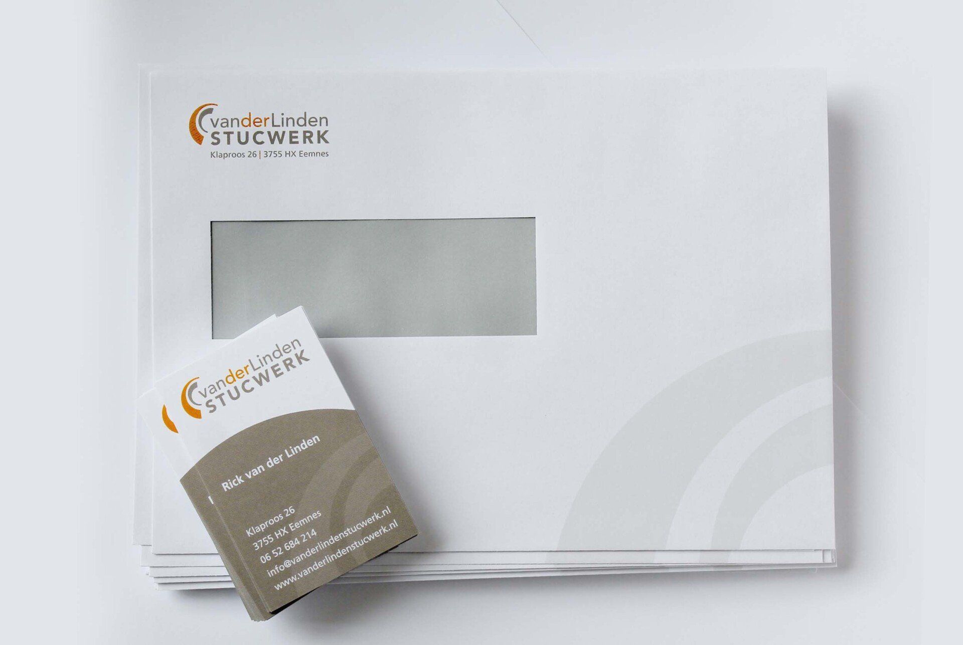 Een witte zakelijke envelop met een venster en een bijpassend visitekaartje met logo, bovenop een stapel.