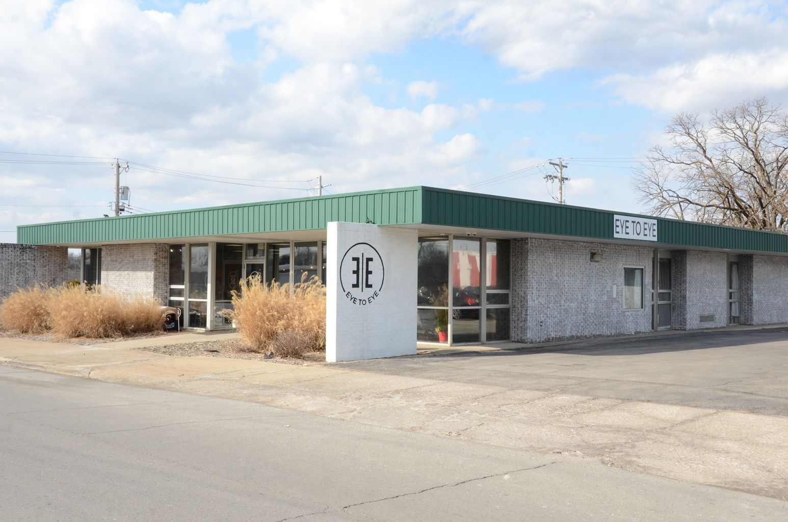 Single-story stone storefront. Eye to eye logo present on stone wall and green roof trim and glass doors.