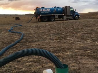 Blue water tanker truck in a dry field, with a hose stretched across the ground at sunset.
